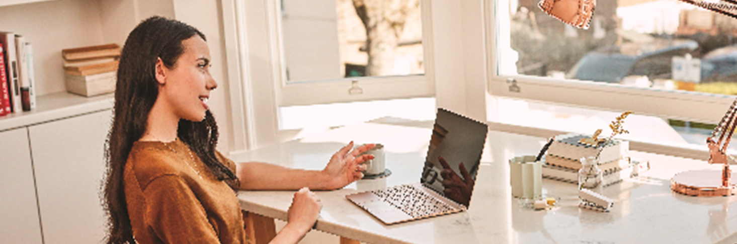 A person at a desk with a laptop, holding a cup.