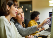 Two female developers work cooperatively on a desktop screen